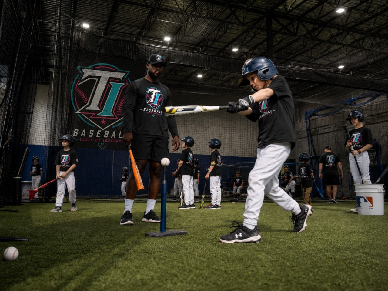 Coach working with a group of young TI Baseball Academy players on tee work at B360 indoor turf